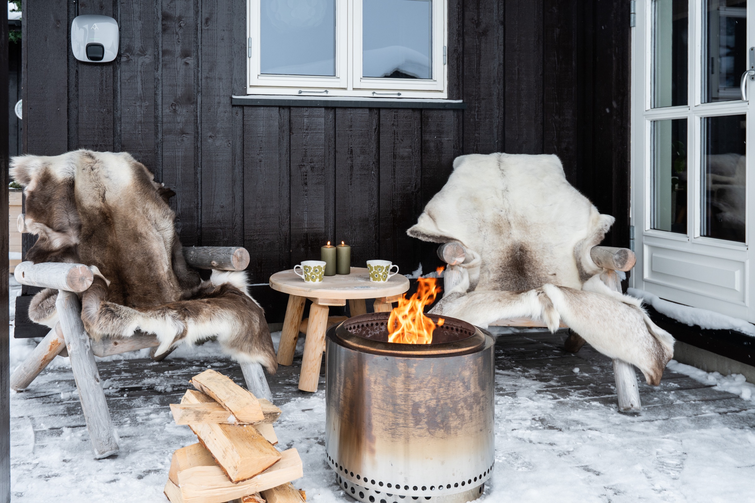 Lun uteplass med to stoler, bålpanne og ved utenfor hytta